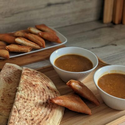 A rustic still life of traditional flatbread, savory samosas, and bowls of rich soup in a cozy setting.